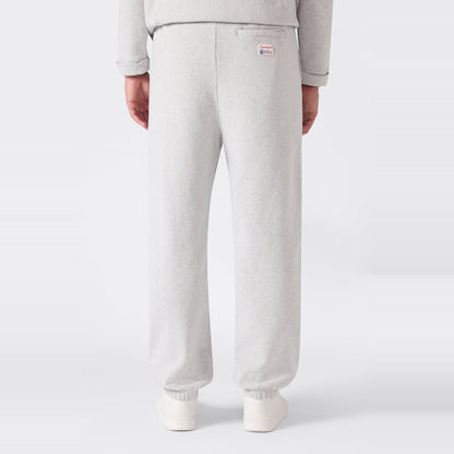 A person is shown from the back wearing Men’s Knitted Elastic Cuff Pants by Champion in light gray, paired with a matching sweatshirt. These trousers feature a loose fit, elastic cuffs, and a small logo patch on the right side near the waistband. Crafted from heavyweight fleece for comfort, the set stands out against a plain white background.
