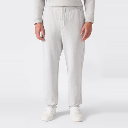 A person is shown from the waist down wearing Champion Men’s Knitted Elastic Cuff Pants in light gray, paired with white sneakers, standing against a plain white background.