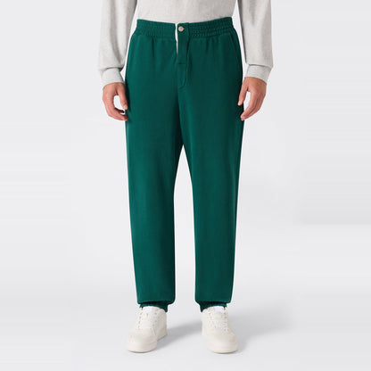 A person wearing Champion Men’s Knitted Elastic Cuff Pants in green, paired with a light gray Reverse Weave fleece sweatshirt and white sneakers, stands against a plain white background.