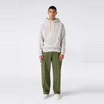 A man stands facing forward against a plain white background, wearing a relaxed fit Men’s Knitted Hooded Sweatshirt by Champion in light gray, paired with olive green pants and white shoes.