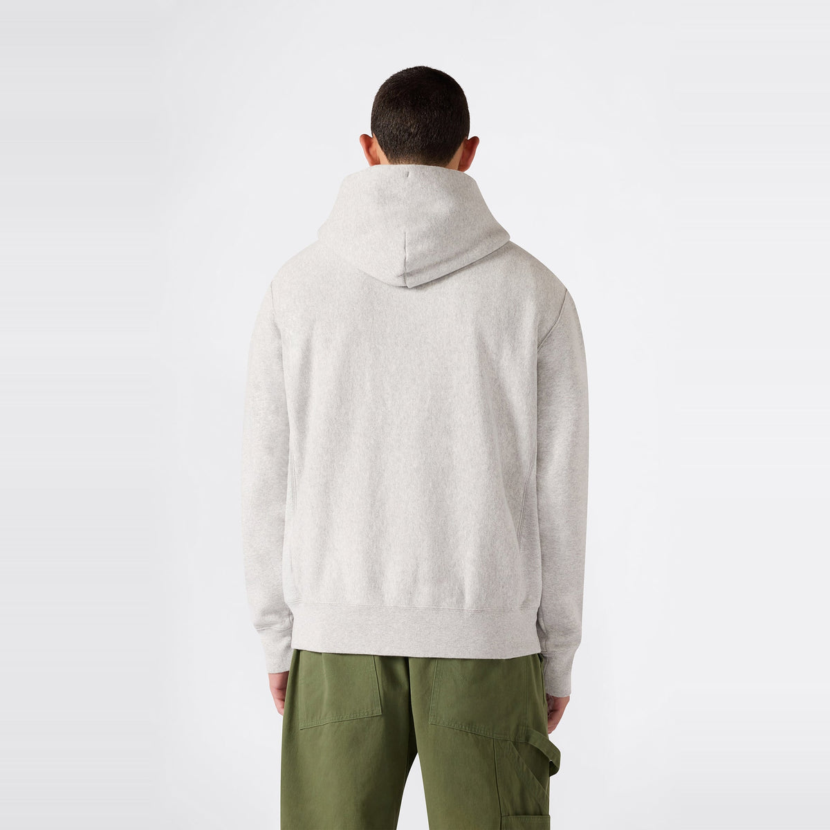 A person facing away, dressed in the Champion Men’s Knitted Hooded Sweatshirt in light gray and olive green cargo pants, stands against a plain white background.