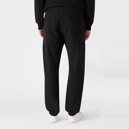 A person is shown from the back against a plain light background, wearing black Champion Men’s Knitted Elastic Cuff Pants—designed in a classic sportswear fleece style with an elastic waistband and single back pocket—and white shoes.