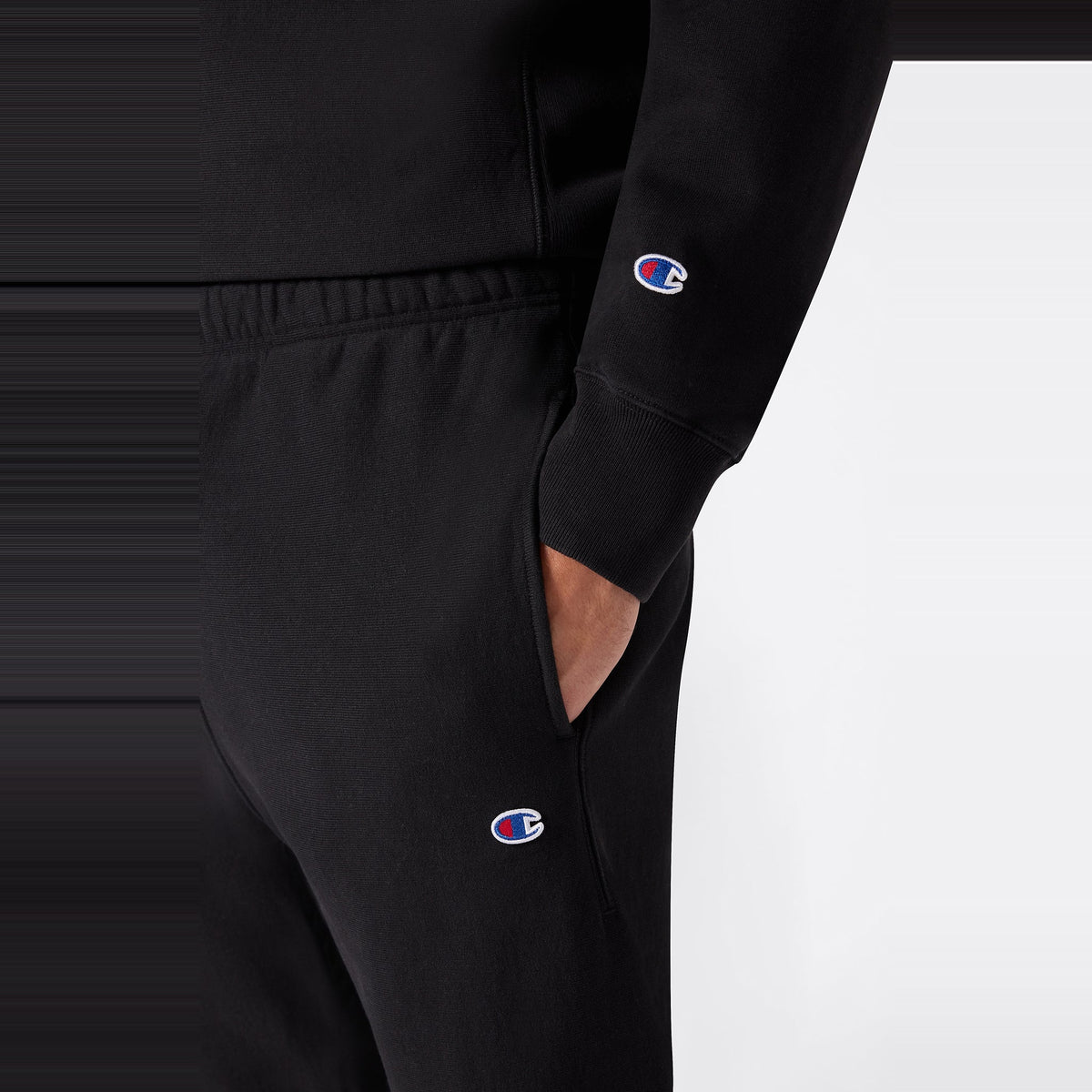 A person wearing a black sweatshirt and Champion Men’s Knitted Elastic Cuff Pants, standing with one hand in their pocket against a plain background.