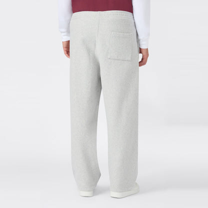 A person wearing light gray Champion Men’s Knitted Wide Leg Pants, featuring a single back pocket, paired with a white shirt and a maroon vest, is shown standing against a plain white background with their back facing the camera.