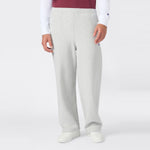 A person is shown from the waist down wearing Champion Men’s Knitted Wide Leg Pants in light gray, paired with a white long-sleeve shirt, a red vest, and white sneakers, standing against a plain white background.