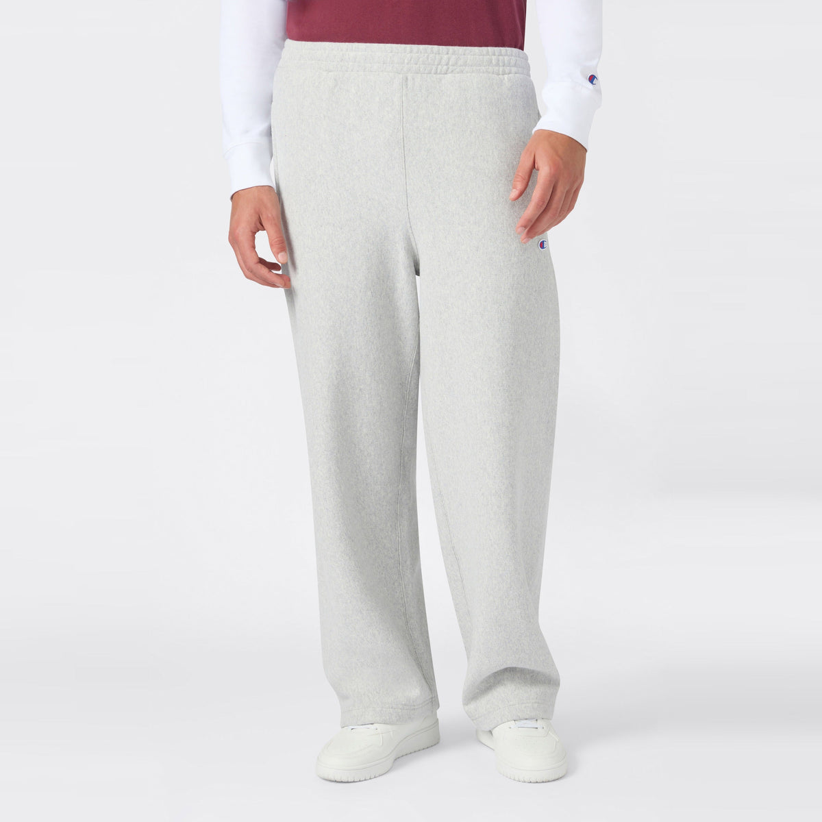 A person is shown from the waist down wearing Champion Men’s Knitted Wide Leg Pants in light gray, paired with a white long-sleeve shirt, a red vest, and white sneakers, standing against a plain white background.