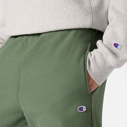 A person wearing an off-white sweatshirt and green Champion Men’s Knitted Wide Leg Pants, both featuring a small embroidered Champion logo, with their hand in the pocket.