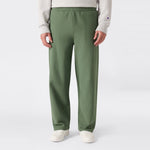 A person is shown from the waist down, standing against a plain light background and wearing loose-fitting green Champion Men’s Knitted Wide Leg Pants, a light gray sweatshirt, and white sneakers.