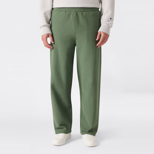 A person is shown from the waist down, standing against a plain light background and wearing loose-fitting green Champion Men’s Knitted Wide Leg Pants, a light gray sweatshirt, and white sneakers.
