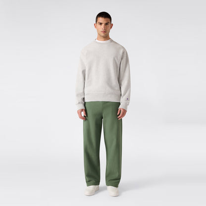 A man stands facing forward against a plain light gray background, wearing a light gray sweatshirt, white shoes, and green Champion Men’s Knitted Wide Leg Pants.