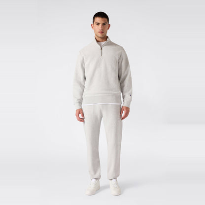 A man stands facing forward wearing a light gray Champion Men’s Knitted Half Zip Sweatshirt, matching sweatpants, a white undershirt, and white sneakers against a plain white background.