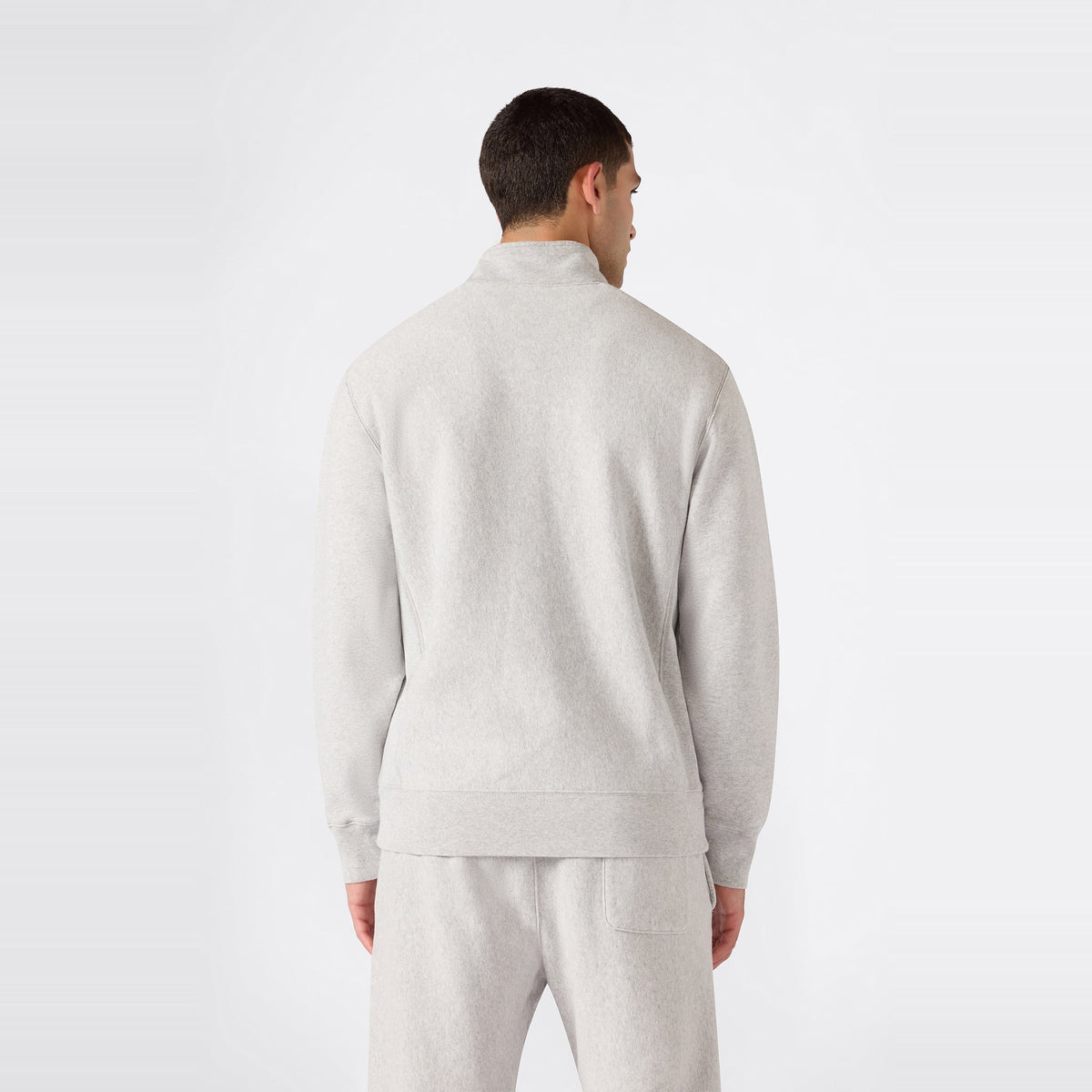 A person wearing a light gray Champion Men’s Knitted Half Zip Sweatshirt and matching sweatpants stands facing away, displaying the back of the outfit against a plain white background and highlighting this classic fleece sportswear look.