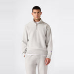 A person stands against a plain background wearing the Champion Men’s Knitted Half Zip Sweatshirt in light gray, styled with matching sweatpants. Crafted from cozy fleece sportswear fabric, the outfit features a relaxed fit and is paired with a casual expression.