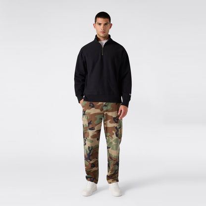 A person stands facing forward wearing a black Champion Men’s Knitted Half Zip Sweatshirt, camouflage cargo pants, and white sneakers against a plain light gray background.
