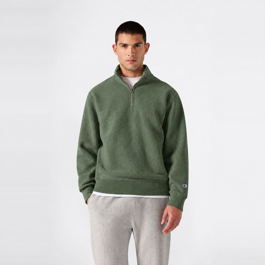 A person wears a green Men’s Knitted Half Zip Sweatshirt by Champion over a white t-shirt and light gray sweatpants, standing against a plain white background.