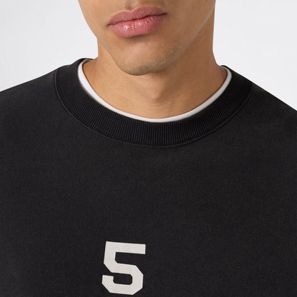 Here’s a revised version of your sentence using the provided product data: A close-up of a person wearing the Champion Men’s Knitted Crewneck Sweatshirt (Reversible + Vintage Wash) in black, featuring a white number 5 and layered over a white crew-neck shirt. Only the lower half of their face and upper torso are visible, highlighting the classic Reverse Weave fleece texture.