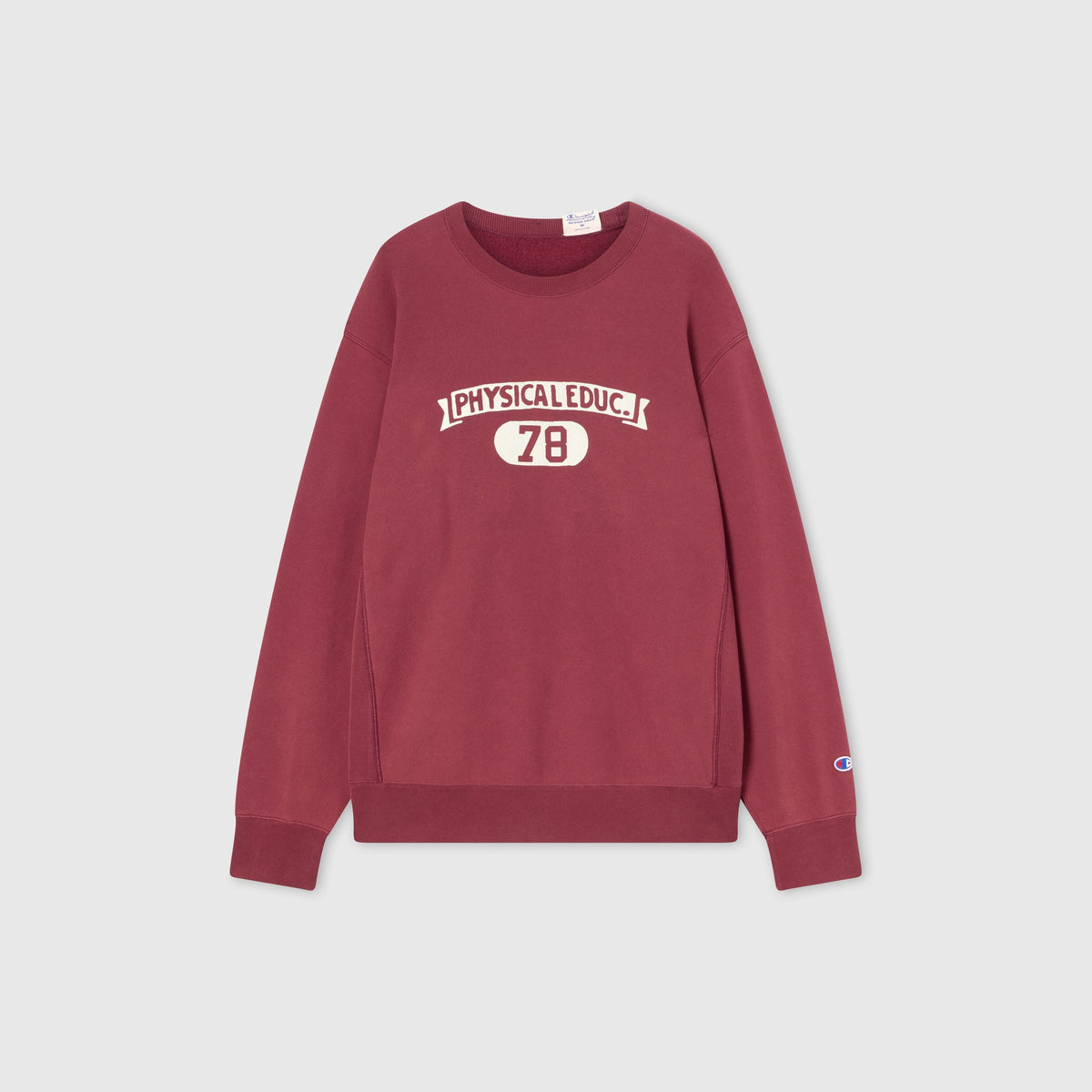 A maroon Champion Men’s Knitted Crewneck Sweatshirt (Reversible + Vintage Wash) featuring “PHYSICAL EDUC. 78” in white lettering on the front and a small Champion logo on the left sleeve, laid flat on a plain light gray background.