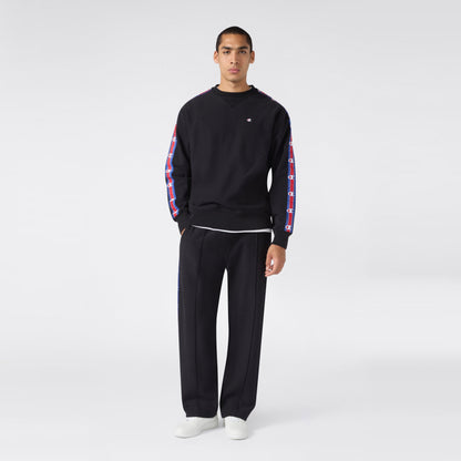 A person stands facing forward, wearing a black sweatshirt with patterned stripes on the sleeves, paired with Champion Men’s Knitted Straight Hem Pants in black featuring matching stripes, and white sneakers, against a plain light background.