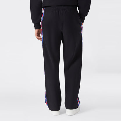 Back view of a person wearing black Champion Men’s Knitted Straight Hem Pants featuring red, white, and blue logo tape along the sides, paired with a matching black sweatshirt and white sneakers against a plain light gray background—an ideal option for men’s sportswear.