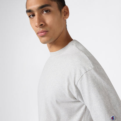 A man wearing a light gray Champion Men’s Knitted T-Shape Tee faces the camera against a plain white background, highlighting this classic piece of men’s sportswear.
