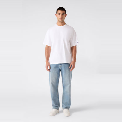 A person stands facing forward, wearing the Champion Men’s Knitted T-Shape Tee, paired with light blue jeans and white sneakers, against a plain light gray background.