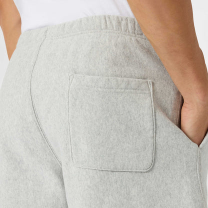Close-up of a person wearing Champion Men’s Knitted Shorts in light gray, with one hand in the side pocket. Inspired by classic men’s sportswear style, the shorts feature a visible back patch pocket and an elastic waistband. The person is also wearing a white shirt.