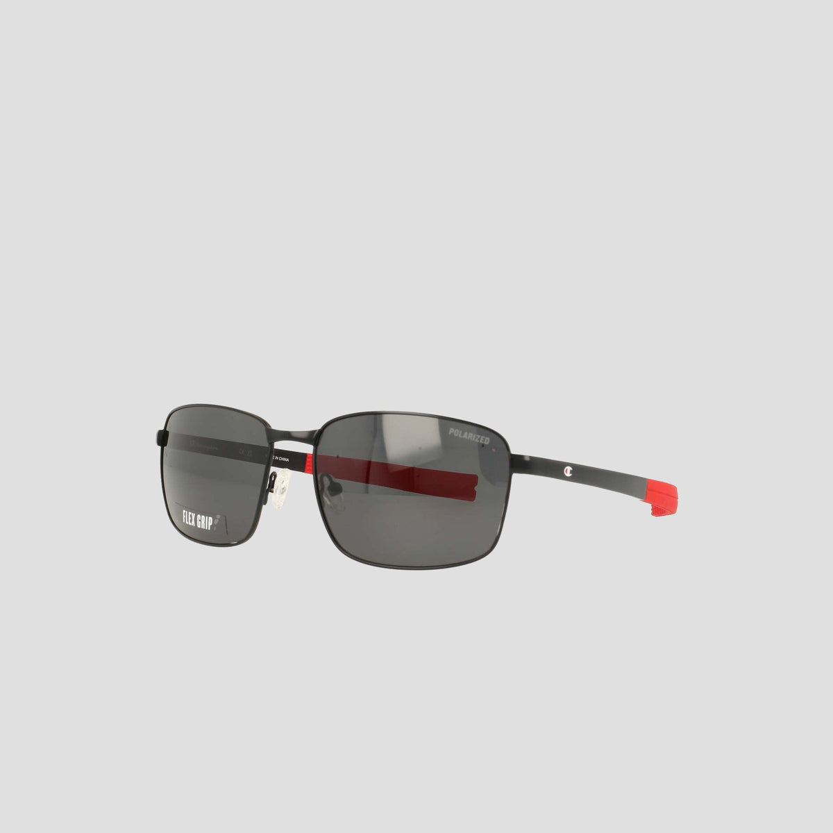 Men’s Champion Polarized Stainless ST-Shirtl Flex Grip Tip sunglasses feature a sleek rectangular black frame with thin black and red arms, a "Polarized" label on one lens, and are designed for active lifestyles. The retainer frame stands out against a plain light gray background.