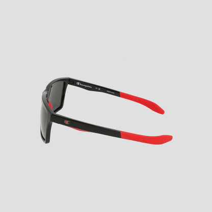 Men's Polarized Grilamid Flex Grip Tip - Medium sunglasses by Champion shown from a side angle on a light gray background. These sunglasses feature a black frame with red arms, and the inside of the left arm displays the Champion logo and size details in white text. Crafted from lightweight TR90 material, they are designed for comfort and durability.