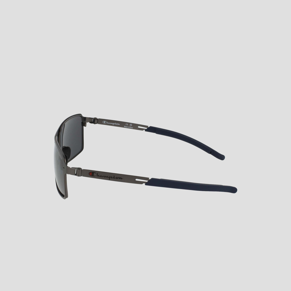 Side view of Champion Men's Polarized Stainless ST-Shirtl Comfort Fit sunglasses, black with metal arms and navy blue adjustable rubber tips, featuring the Champion logo on the left temple, on a light gray background.
