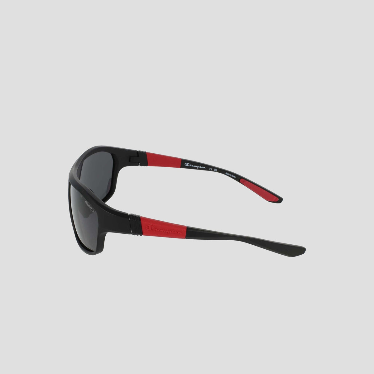 Men’s Polarized Comfort Fit - Large by Champion, black sunglasses with red accents on the arms, shown from a side angle. Featuring a durable TR90 frame and adjustable rubber tips for enhanced comfort, the arms are marked with a white Champion logo. The polarized dark lenses are set against a light gray background.