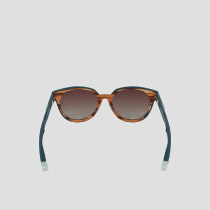 Champion Women's Polarized Retainer Round sunglasses feature brown tortoiseshell round frames, dark gradient polarized lenses, and teal-blue arms with white tips, shown against a light gray background.