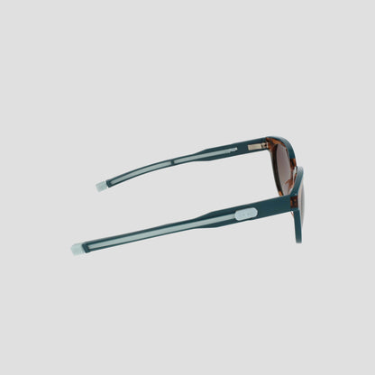 Side view of Champion Women's Polarized Retainer Round eyewear in teal with brown-tinted lenses and silver arm accents, displayed against a plain white background.