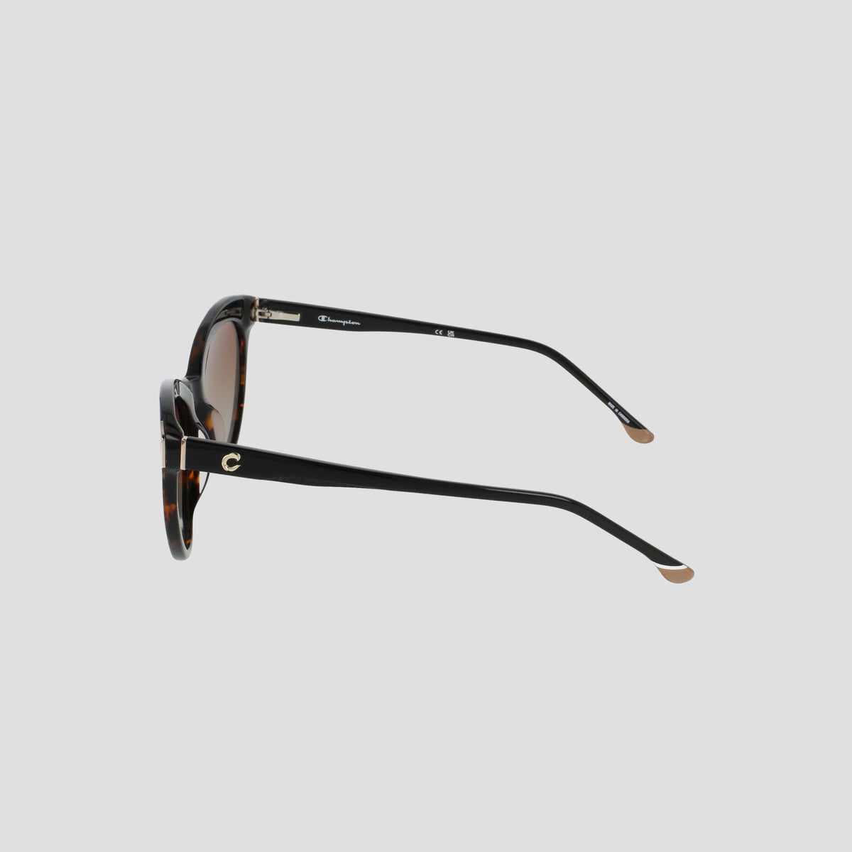 Side view of the Champion Women's Polarized Cateye sunglasses featuring a tortoiseshell design, black arms, gold accents, and brown-tinted lenses, displayed on a plain light gray background. The RX-able frame offers versatility for prescription wearers.