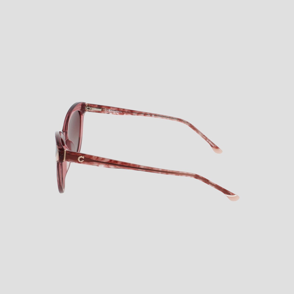 Side view of the Champion Women's Polarized Cateye sunglasses in pink, featuring round, RX-able translucent frames and lightly tinted lenses. The slim arms showcase a subtle gold C detail near the hinge, set against a plain white background.