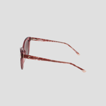 Side view of the Champion Women's Polarized Cateye sunglasses in pink, featuring round, RX-able translucent frames and lightly tinted lenses. The slim arms showcase a subtle gold C detail near the hinge, set against a plain white background.