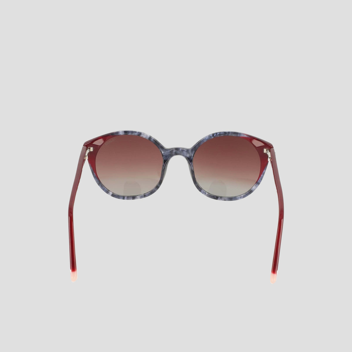 The Champion Women's Polarized Flirty Round sunglasses are displayed against a plain light gray background, featuring marbled gray handmade acetate frames, red gradient lenses, and coordinating red arms. These unique shades blend retro-inspired accents with modern sophistication.