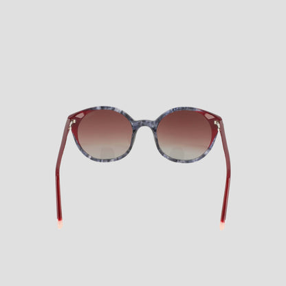 The Champion Women's Polarized Flirty Round sunglasses are displayed against a plain light gray background, featuring marbled gray handmade acetate frames, red gradient lenses, and coordinating red arms. These unique shades blend retro-inspired accents with modern sophistication.