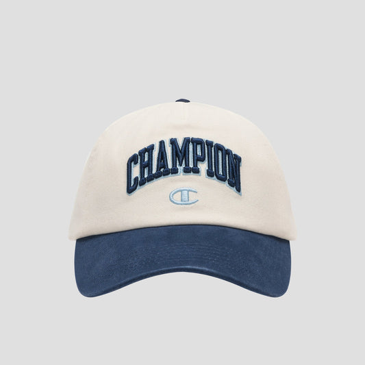 A beige and navy blue Amor Adjustable Baseball Cap by Champion, crafted from washed cotton twill and featuring “CHAMPION” embroidered in dark blue lettering on the front with a small Champion logo below, photographed on a plain gray background—showcasing true Champion authenticity.