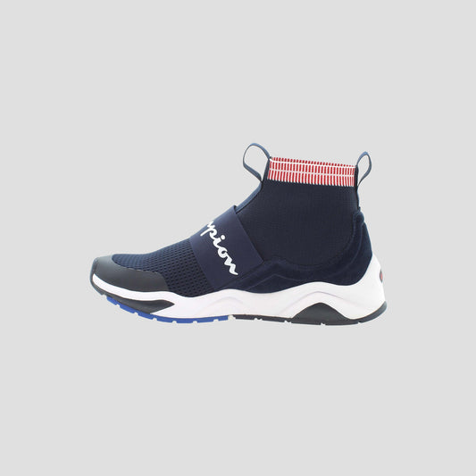 The Champion Men's Rally Pro is a navy blue slip-on sneaker featuring a cushioned insole, white sole, black toe cap, red and white striped ankle collar, and a white script logo on the side, shown on a light gray background.