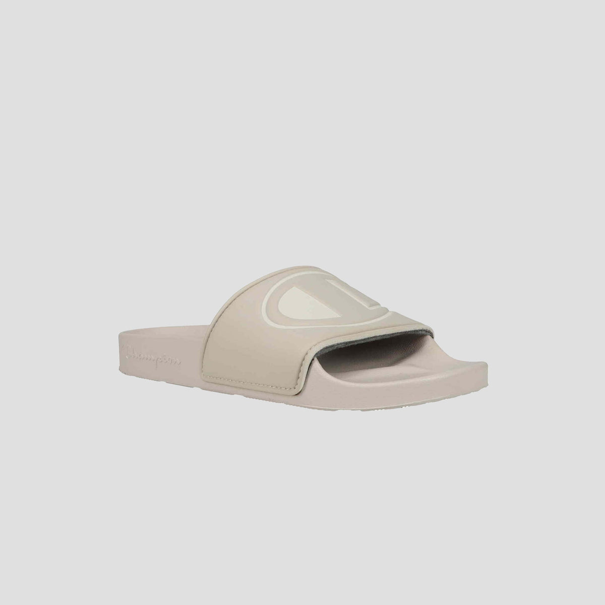 The Champion Women's IPO Slide is a beige sandal featuring an open toe, wide strap with large embossed C logo, flat sole, and lightweight comfort—perfect for everyday wear.