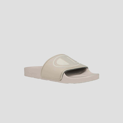 The Champion Women's IPO Slide is a beige sandal featuring an open toe, wide strap with large embossed C logo, flat sole, and lightweight comfort—perfect for everyday wear.