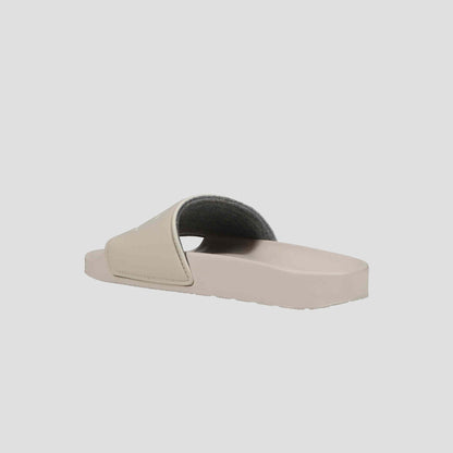 The Champion Women's IPO Slide, shown from the side on a light gray background, features a beige wide strap, grey lining, and contoured footbed for lightweight everyday comfort.