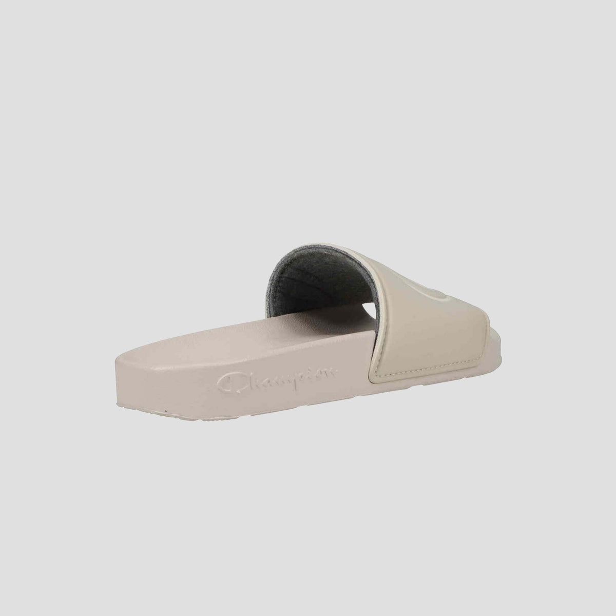 The Champion Women’s IPO Slide in beige features an open toe, thick strap, contoured footbed, and logo-embossed sole, providing lightweight comfort. Viewed from the side and slightly behind.