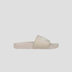 The Champion Women's IPO Slide is a beige sandal with a wide, raised-logo strap, lightweight comfort, contoured footbed, and textured sole, shown on a plain light gray background.