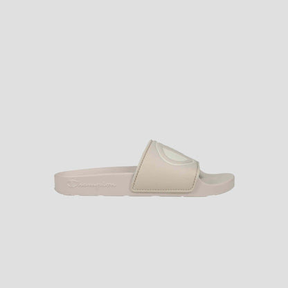 The Champion Women's IPO Slide is a beige sandal with a wide, raised-logo strap, lightweight comfort, contoured footbed, and textured sole, shown on a plain light gray background.
