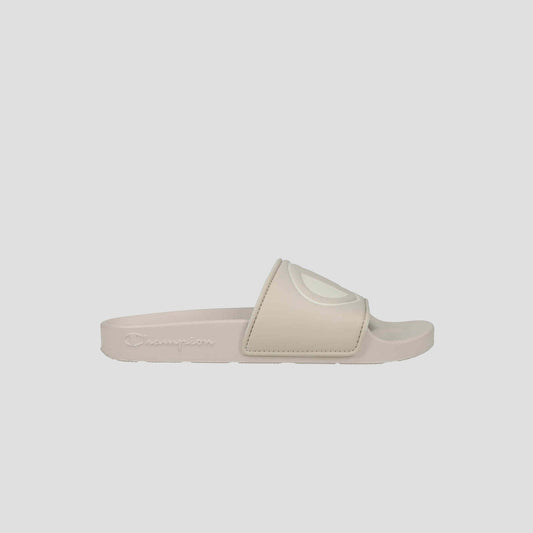 The Champion Women's IPO Slide is a beige sandal with a wide, raised-logo strap, lightweight comfort, contoured footbed, and textured sole, shown on a plain light gray background.