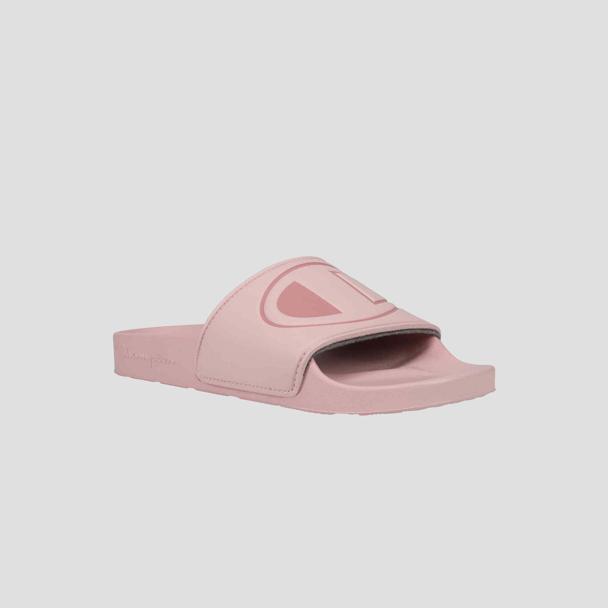 The Champion Women's IPO Slide is a light pink sandal with a wide strap and raised logo, featuring an open toe, contoured footbed for comfort, and flat sole. The background is plain and light-colored.