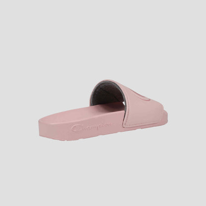 The Champion Women's IPO Slide features a light pink open toe design, wide strap, contoured footbed, and embossed logo on the sole. Displayed on a light gray background. Perfect slides for women.