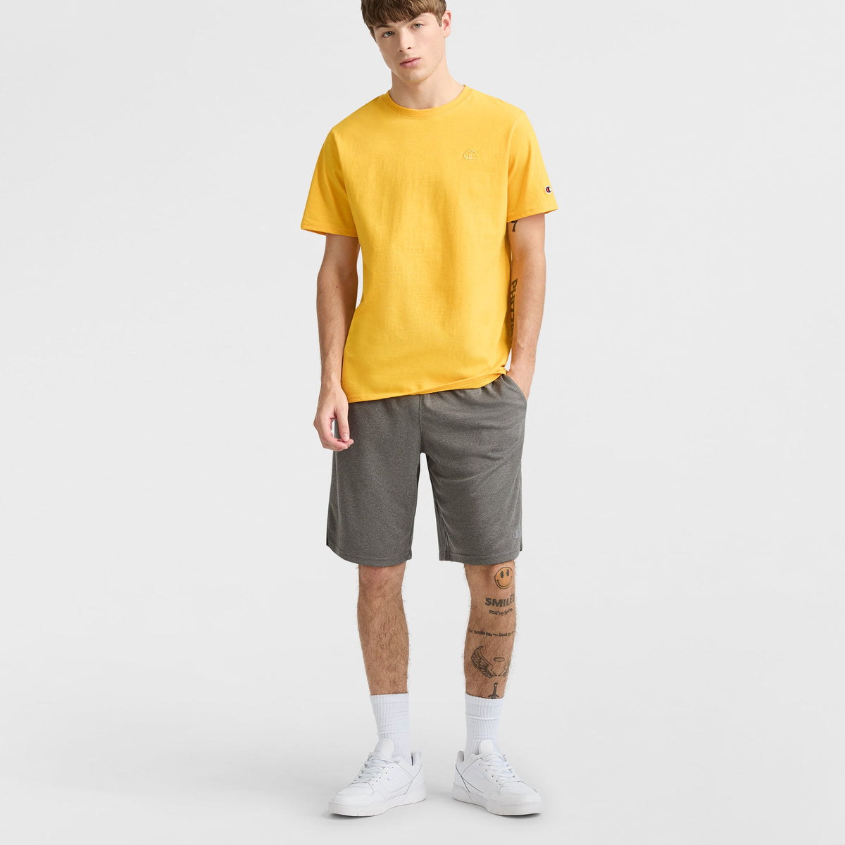 A man wearing a yellow t-shirt and grey 10″ Moisture Wicking, Sport Shorts by Champion with white socks and sneakers.