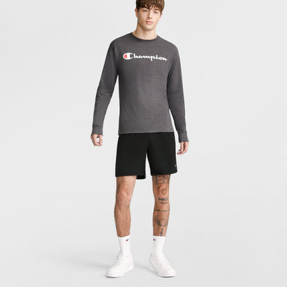A young man with tattoos on his right leg wears Champion 10" Moisture Wicking Sport Shorts, a gray long-sleeve Champion shirt, white socks, and white sneakers against a plain background, showing a neutral expression.